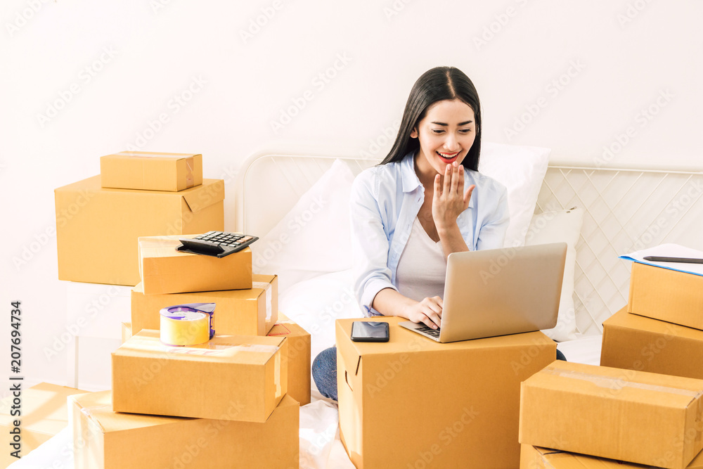 Young woman freelancer working and use laptop computer with cardboard box on bed at home - SME business online and delivery concept Young woman freelancer working and use laptop computer with cardboard box on bed at home - SME business online and delivery concept