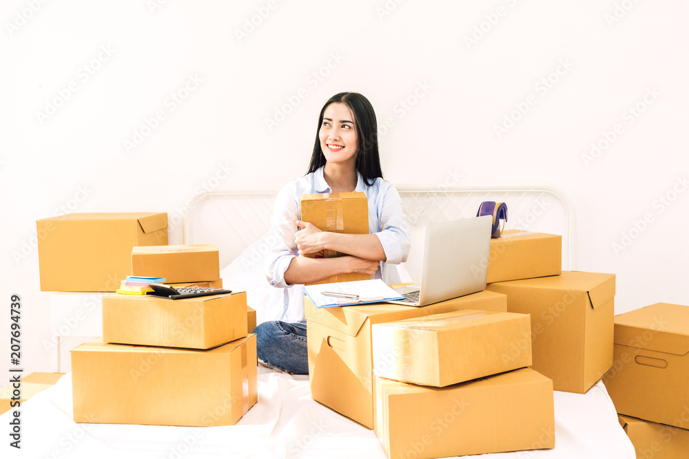 Young woman freelancer working and holding cardboard box on bed at home - SME business online and delivery concept Young woman freelancer working and holding cardboard box on bed at home - SME business online and delivery concept