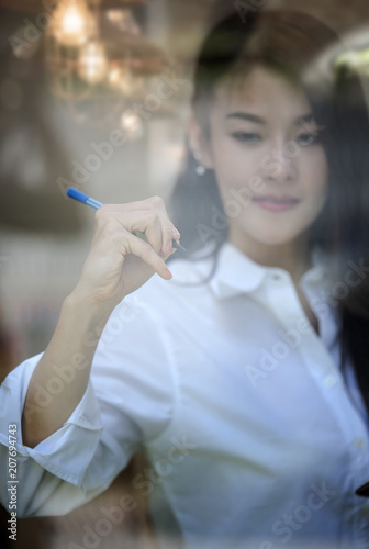 young Caucasian businesswoman writing or drawing something on blank glass board