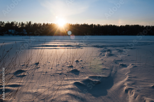 Beautiful winter scene. Sunset at the frozen lake covered with snow.