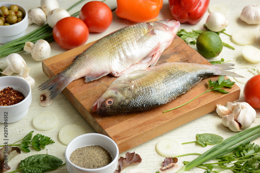 Fresh uncooked dorado or sea bream fish with lime, herbs, vegetables and spices on rustic wooden board over white backdrop, top view. Healthy food or diet nutrition concept. Fresh uncooked dorado or sea bream fish with lime, herbs, vegetables and spices on rustic wooden board over white backdrop, top view. Healthy food or diet nutrition concept.