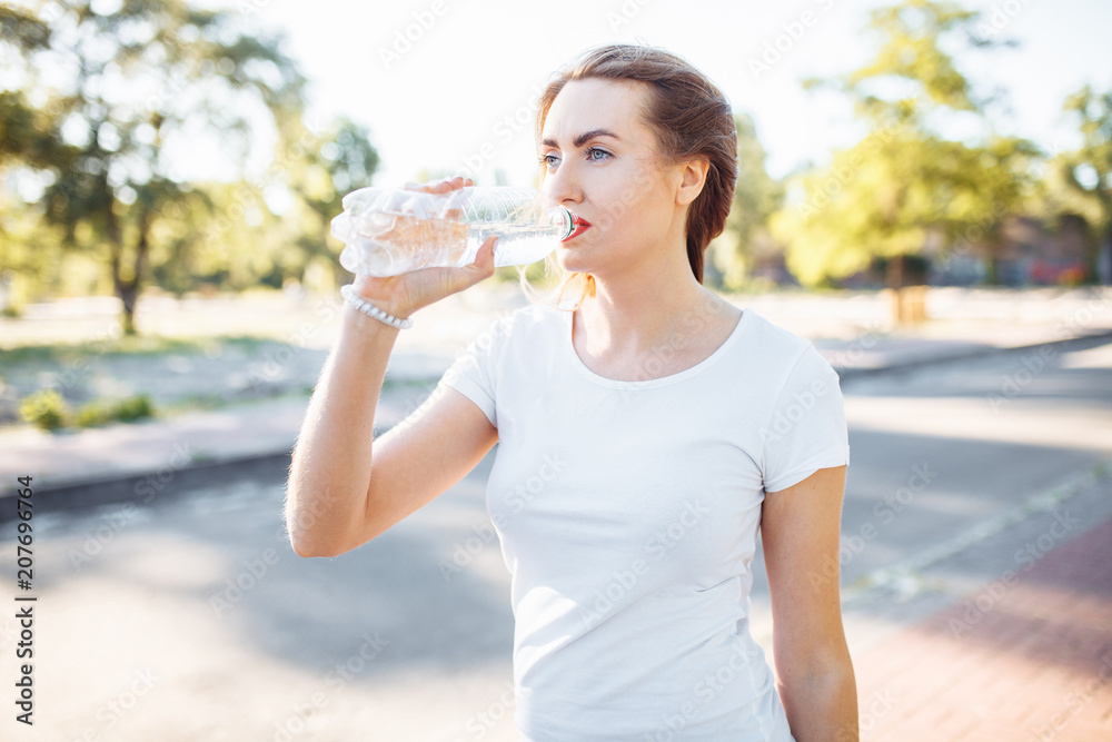 Young sports girl, drinking water from the bottle, after a hard workout, can be used for advertising, text insertion Young sports girl, drinking water from the bottle, after a hard workout, can be used for advertising, text insertion