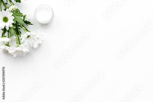 Natural emollient chamomile cream. White cream in small jar near chamomile flowers on white background top view copy space