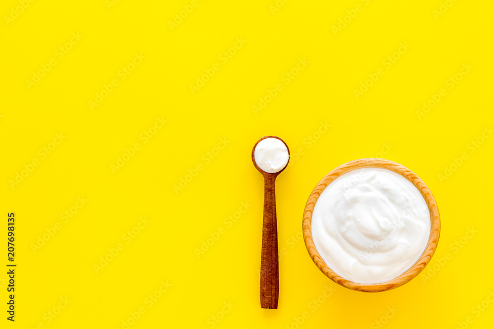 Healthy product, healthy meal. Greek yogurt in brown bowl near spoon on yellow background top view copy space Healthy product, healthy meal. Greek yogurt in brown bowl near spoon on yellow background top view copy space