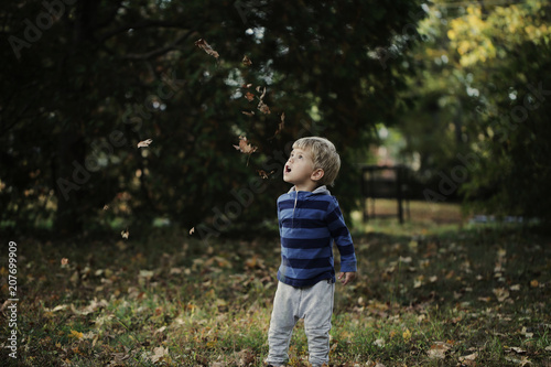 Little boy, playing in the rain in autumn park, leaves around him