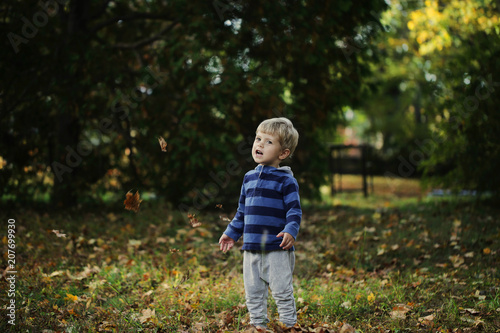 Little boy, playing in the rain in autumn park, leaves around him