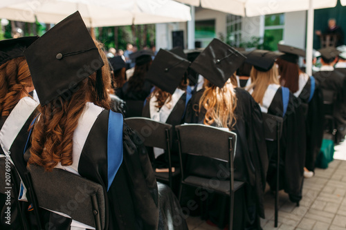 Fotografie Successful graduates in academic dresses, at graduation, sitting in the form of