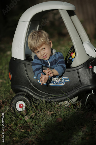 Blonde Little boy driving big toy police car outdoors