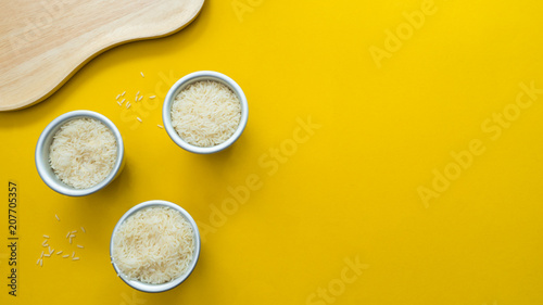 White rice in silver cup and wood plate on yellow background