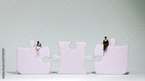 Three pieces of puzzle and a miniature man and woman sitting on them. Three empty pieces of puzzle. photo