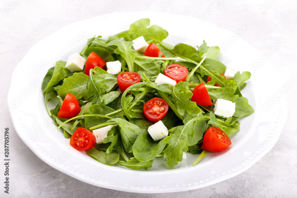 Salad with arugula, baby spinach, feta cheese and tomato cherry on white plate. Menu concept Salad with arugula, baby spinach, feta cheese and tomato cherry on white plate. Menu concept