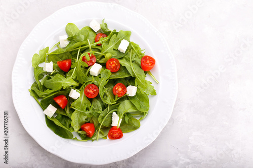 Salad with arugula, baby spinach, feta cheese and tomato cherry on white plate. Menu concept