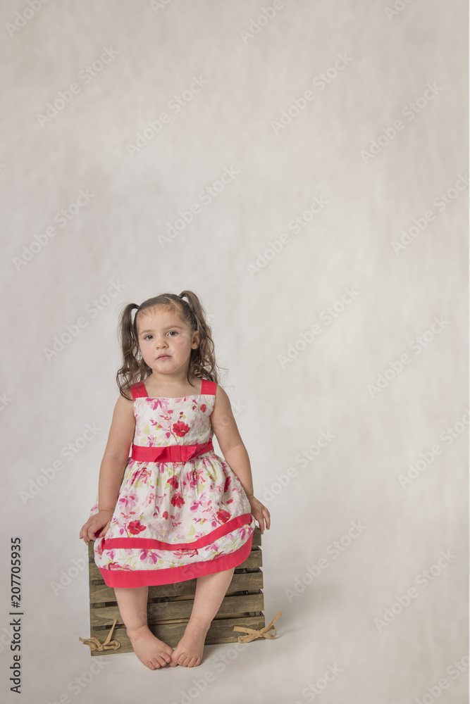 Toddler girl in bare feet with sad expression, sitting on wooden box Toddler girl in bare feet with sad expression, sitting on wooden box