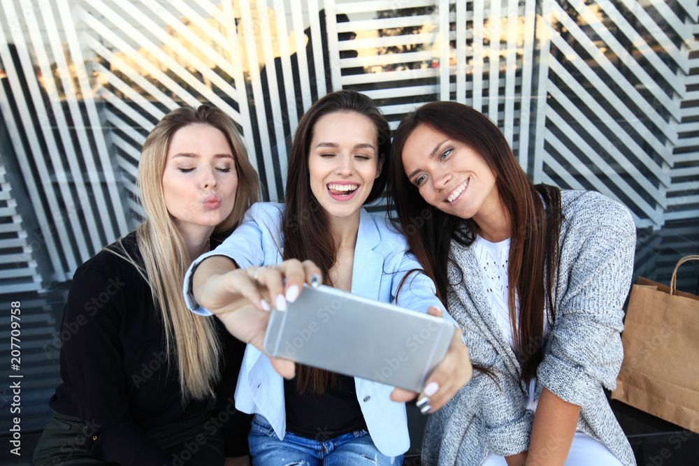 Three women taking a selfie while shopping in a clothing store. They are happy and smiling at camera. Shopping concept, also related to social media addiction.