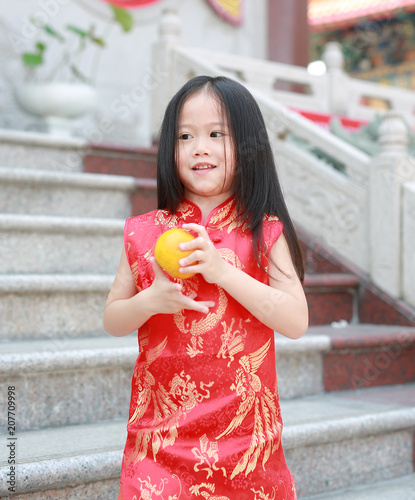 Cute asian kid girl in Traditional Chinese dress with holding sacred Orange at chinese temple in bangkok thailand, Chinese new year concept.
