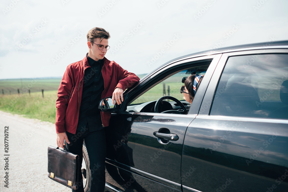 Pretty girl sitting behind the wheel of a black car on the background of a  blue