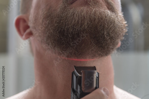 A man of European Russ cuts a beard with an electric trimmer.