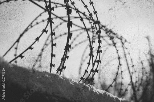 Barbed wire stretches along the concrete wall. Black and white photo photo