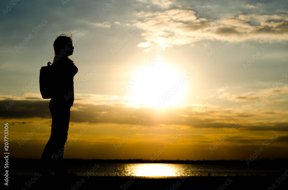 Silhouette of a woman wolking alone at the field during beautiful sunset.