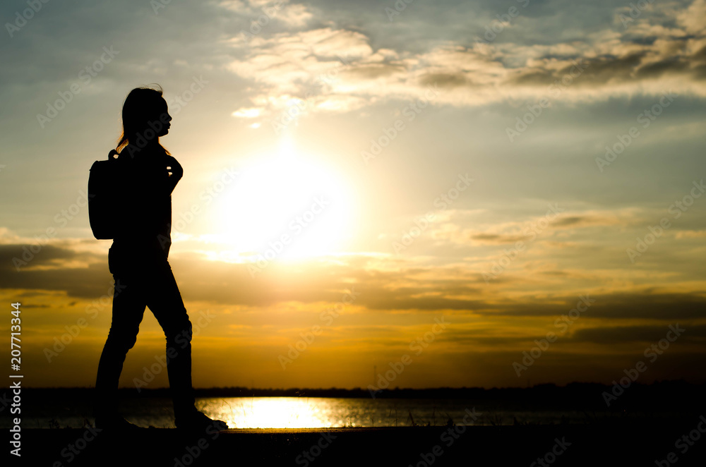 Silhouette of a woman wolking alone at the field during beautiful sunset.