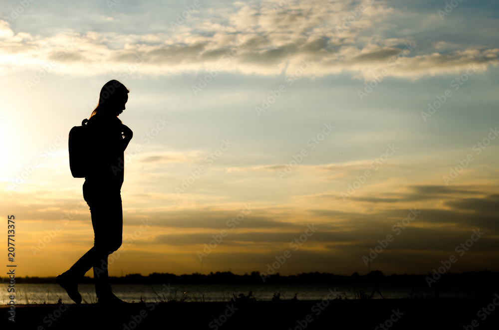 Fototapeta premium Silhouette of a woman wolking alone at the field during beautiful sunset.