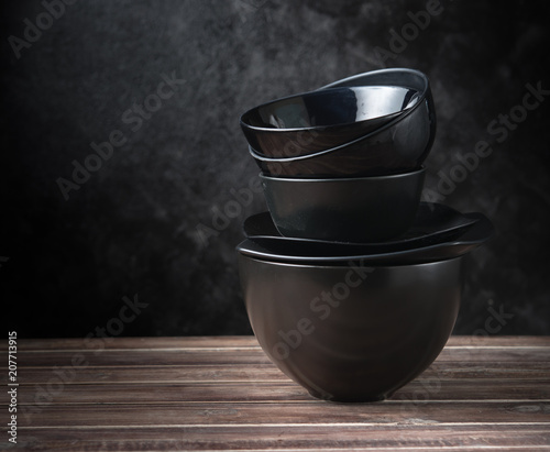 Stack of black ceramic dishware on wood against black cement wall