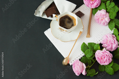 Cup of coffee, roses bunch, notepad, pen, chocoate and phone on black background photo