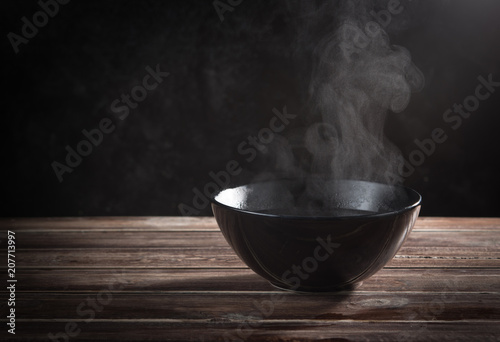 Steam of hot soup with smoke in ceramic bowl against black cement wall