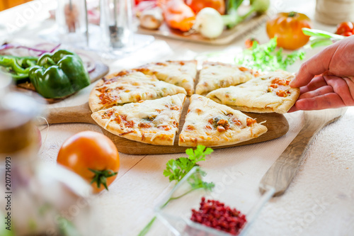 closeup hand taking slice of fresh homemade traditional italian cheese pizza on white wooden table. wallpaper for pizzeria and cooking food concept