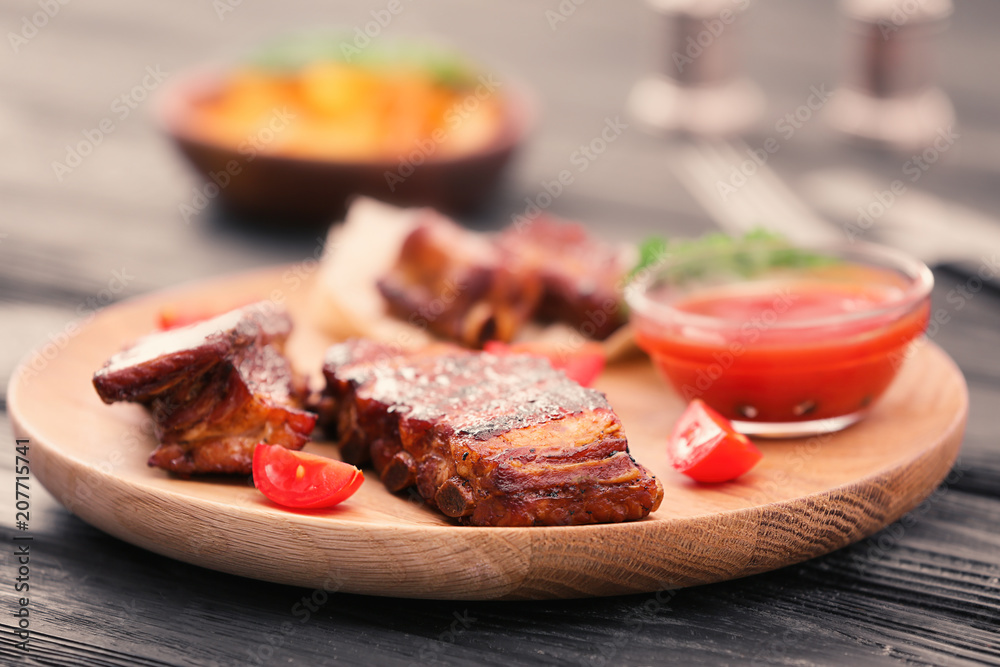 Wooden plate with delicious grilled ribs on table Wooden plate with delicious grilled ribs on table