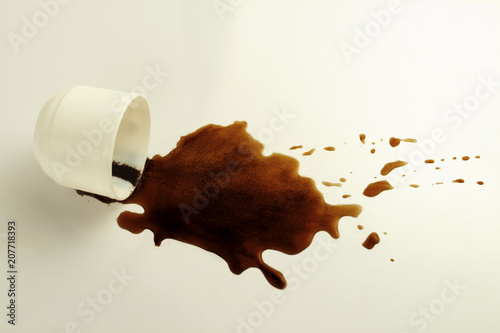 White cup and spilled black coffee on a white background