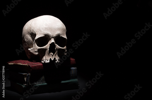 Human skull on old books on black background under beam of light. Dramatic concept.