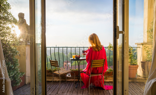 Photography Woman sitting on balcony and overlooking city in morning at sunrise