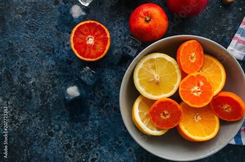 Mix of fresh ripe citrus fruits as blood oranges, mandarines, lemons with ice cubes in a bowl on a blue stone background. © galiyahassan
