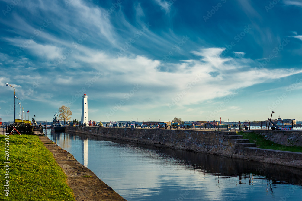 the lighthouse stands on the beach and canal, the blue sky with clouds and reflection in the water