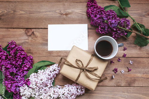 Bouquet of lilac flowers on wooden planks with blank card for text and coffee