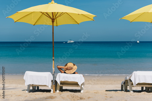 A women sitting on beach chair under colorful yellow beach umbrella with a background of beautiful Andaman sea in Phuket  Thailand