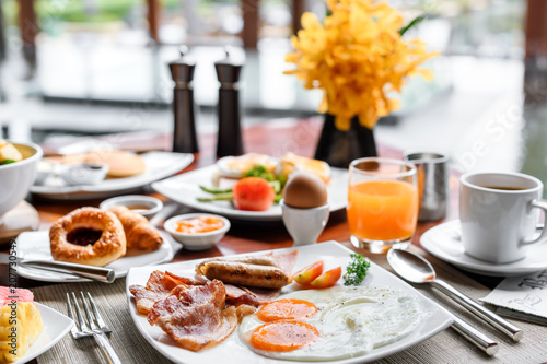 Fotografiet Setting of breakfast includes coffee, fresh orange juice, eggs on table in hotel