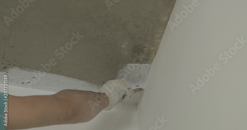 worker painting concrete ceiling into white with brush