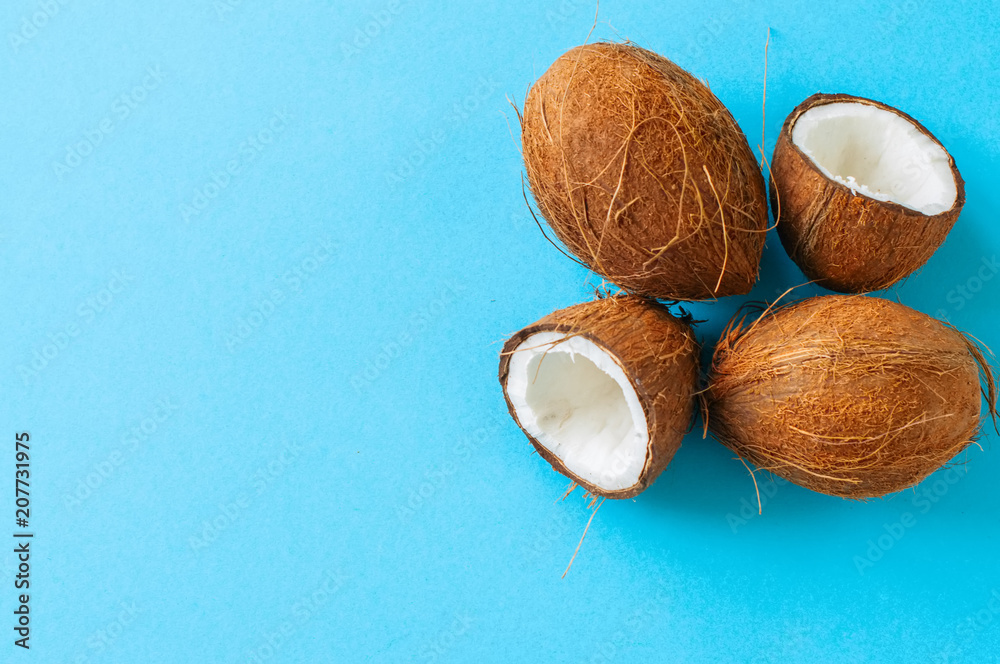 Whole and halfs of coconuts on a blue background. Top view and copy space.