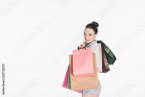 side view of stylish woman with shopping bags looking at camera isolated on white