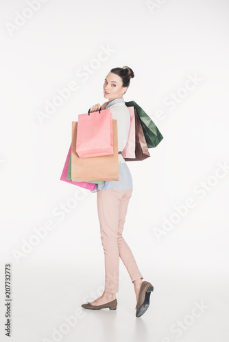 side view of stylish woman with shopping bags looking at camera isolated on white © LIGHTFIELD STUDIOS