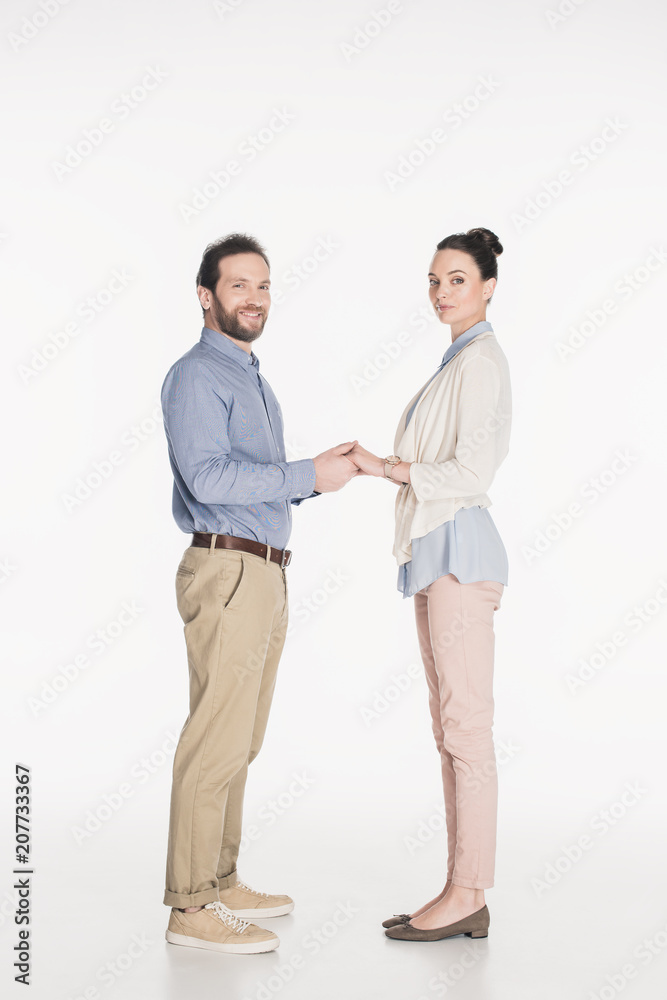 side view of married couple holding hands and looking at camera together isolated on white