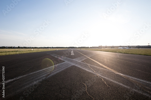 Road in perspective in the plain with horizontal signs to X. Asphalted road with white signs and sun at sunset in the background, effect of light in the lens. Long straight in perspective as airport
