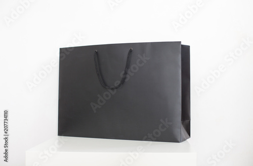 Blank black paper shopping bag on white podium in studio. Advertising and branding, shopping concept.