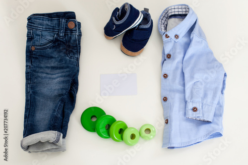 Composition with fashionable classic children clothes and business card on white background Top view shirt, jeans, shoes and accessories, and white business card.