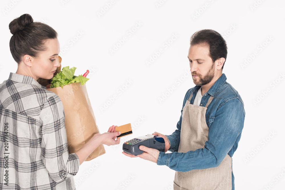 side view of woman with paper package with food giving credit card to shop assistant with cardkey reader isolated on white