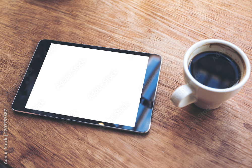 Top view mock up image of black tablet with white blank desktop screen and coffee cup on vintage wooden table in cafe Top view mock up image of black tablet with white blank desktop screen and coffee cup on vintage wooden table in cafe
