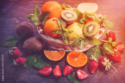 citrus fruits in a basket and strawberries on a wooden background