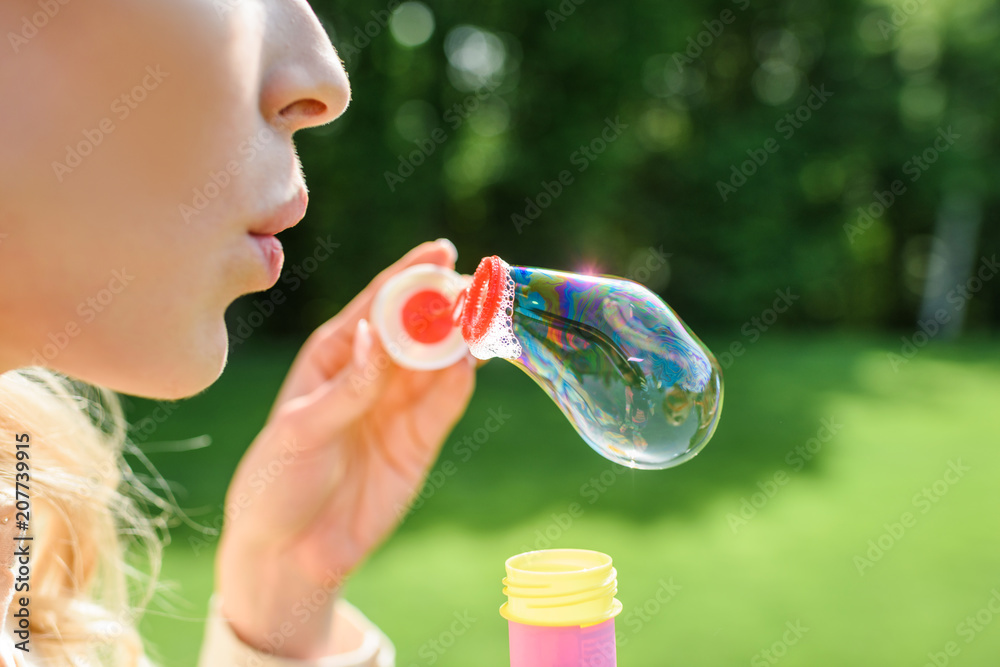 cropped shot of young woman blowing soap bubbles in park